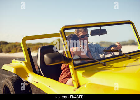 Woman kissing man driving car. Couple on road trip. Romantic caucasian couple on holiday having fun in car. Stock Photo