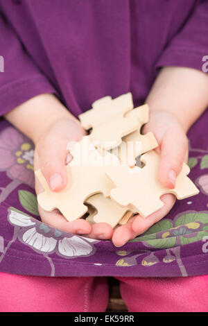 Little girl (5 years) holding pieces of wooden puzzle in her hands. Conceptual image of childhood challenge, cooperation and Stock Photo