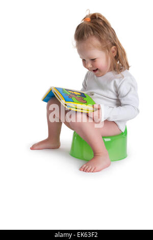 Three year old girl sitting on a potty and reads a picture book on white background Stock Photo