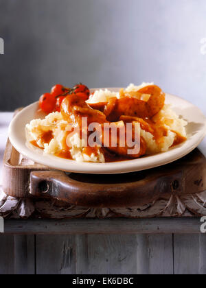 Cooked meal of Cumberland sausages, onion gravy & mashed potatoes served on a plate in a rustic table setting Stock Photo