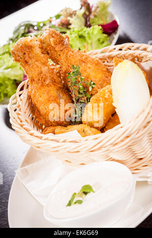 Crispy fried crumbed chicken nuggets in a wicker basket served as a finger food or appetizer with a creamy dip in a bowl alongsi Stock Photo