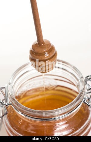 Honey in a glass pot with wooden dipping stick Stock Photo