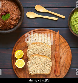 Overhead shot of wholegrain bread slices on wooden plate with two rustic bowls of homemade vegetable spreads Stock Photo