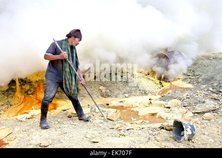 BANYUWANGI, EAST JAVA NOV 12:Sulphur miner using metal crowbar to prise off hardened sulphur to be collected and sold Stock Photo