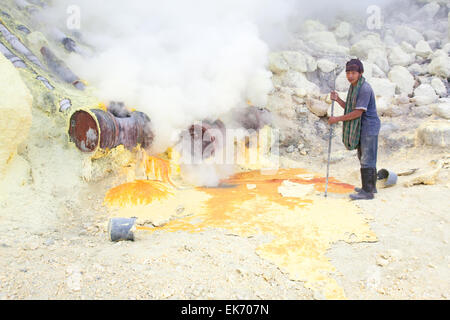 BANYUWANGI, EAST JAVA NOV 12 : Sulphur miner using metal crowbar to prise off hardened sulphur to be collected and sold to tradi Stock Photo
