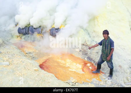 BANYUWANGI, EAST JAVA NOV 12:Sulphur miner using metal crowbar to prise off hardened sulphur to be collected and sold to trading Stock Photo
