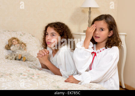 Adorable victorian girls kneeling in their vintage bedroom and praying Stock Photo