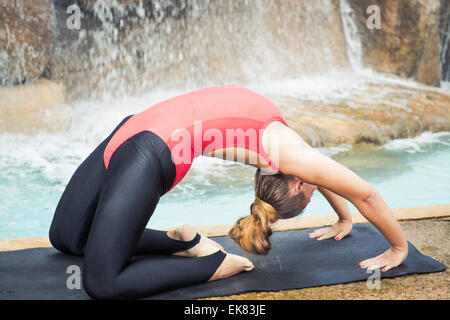 Woman practicing yoga near waterfall. Extended Camel Pose. Utthita Ustrasana Stock Photo