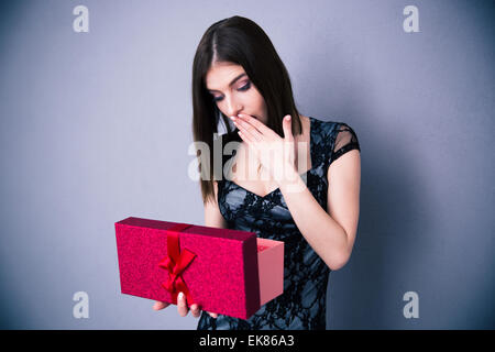 Amazed woman opening gift box over gray background. Wearing in dress. Looking on present Stock Photo
