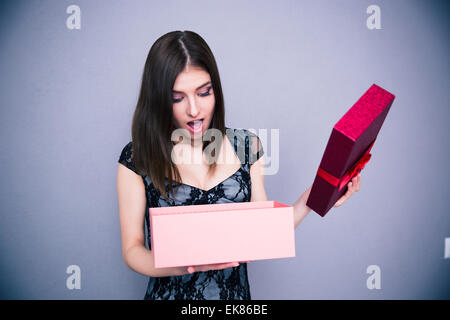 Happy surprised woman opening gift box over gray background. Wearing in dress. Looking on present Stock Photo