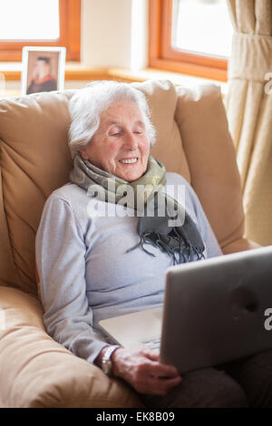 Old lady sitting in armchair using a laptop. Stock Photo