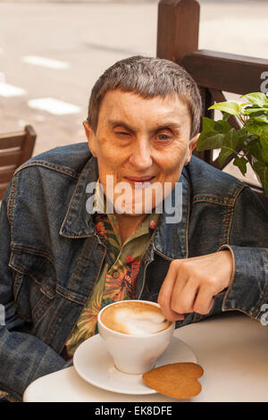 Elderly disabled man with cerebral palsy sitting at outdoor cafe with cup of coffee. Stock Photo