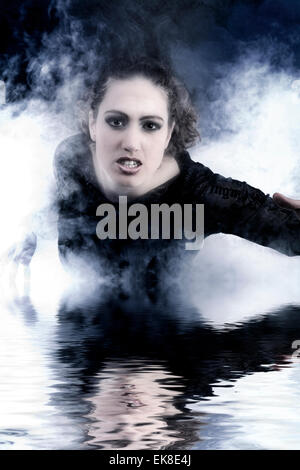 Woman with long curly hair crawling out of smoke Stock Photo