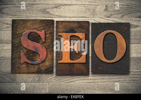 The word "SEO" theme written in vintage, ink stained, wooden letterpress type on a wood grained background. Stock Photo