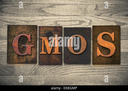 The word 'GMOs' theme written in vintage, ink stained, wooden letterpress type on a wood grained background. Stock Photo