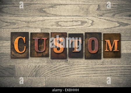 The word "CUSTOM" theme written in vintage, ink stained, wooden letterpress type on a wood grained background. Stock Photo