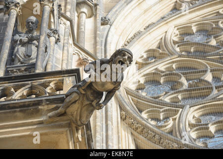 Gargoyle of St. Vitus Cathedral on background of the wall with human sculpture and stone tracery bar Stock Photo