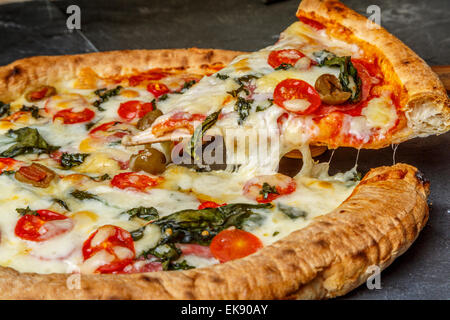 A close up view of a home made thin crust pizza slice with olives tomatoes peppers basil mozzarella cheese, London UK Stock Photo