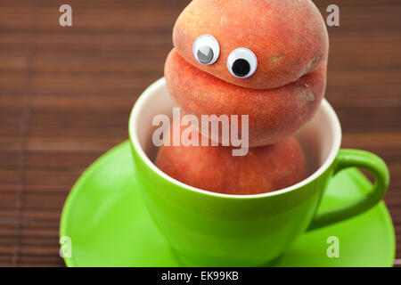 Peach with eyes in the cup and saucer on a bamboo mat Stock Photo
