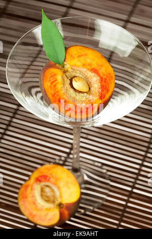 peach with a leaf and a martini glass on a bamboo mat Stock Photo