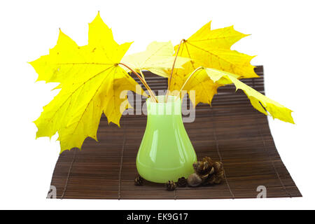 yellow maple leaves and buds in a vase on a bamboo mat Stock Photo