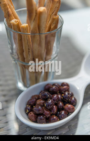 Small black olives in a bowl with breadsticks in a glass tumbler on a table at a bar or restaurant Stock Photo