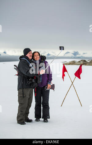 couple taking photograph with selfie stick, Winter Island, Antarctica. Stock Photo