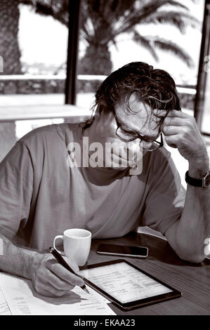 B&W Mature man in holiday setting concentrating on financial statements and business papers along with his iPad Air and iPhone 6 Stock Photo