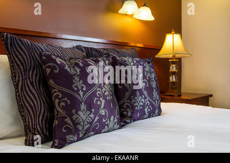 Purple patterned cushion on a bed with a bedside lamp Stock Photo