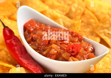 Hot tomato salsa with chili beside and surrounded by cheese flavored nachos (Selective Focus) Stock Photo