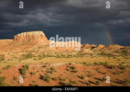 The red sandstone cliffs of Kitchen Mesa at Ghost Ranch can become dramatic when a rainbow appears during a stormy summer day. Stock Photo