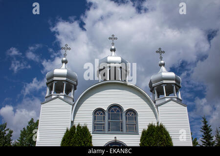 White country church with three crosses or steeples against bright blue summer sky with fluffy white clouds. Stock Photo