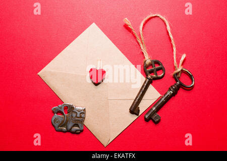 Envelope with heart, two old keys and little monster on a red background. Stock Photo