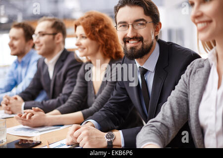 Young businessman sitting among co-workers and looking at camera at conference Stock Photo
