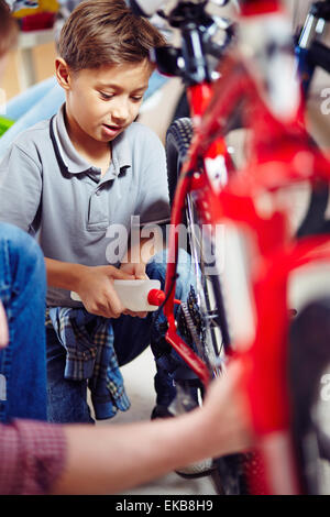 Little boy lubricating bike wheel chain Stock Photo
