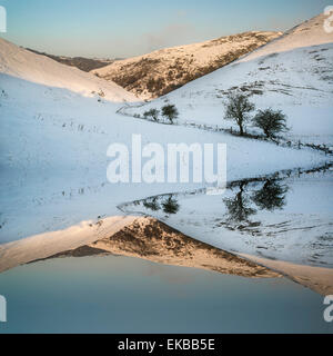 Snow covered Winter countryside sunrise landscape reflected in calm lake Stock Photo