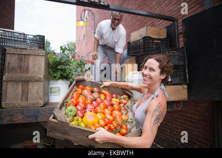 Farmers unloading crates of organic tomatoes outside grocery store Stock Photo