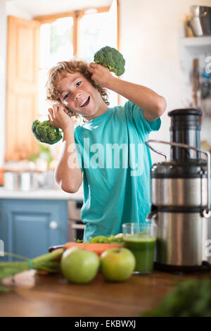 Teenage boy playing with broccoli in kitchen Stock Photo