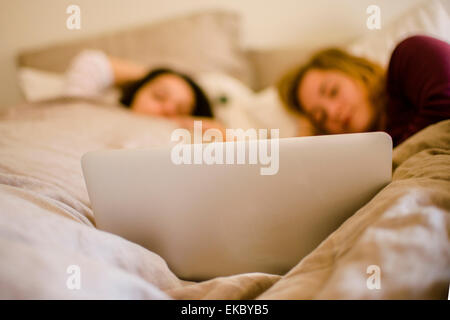 Two young female friends lying in bed looking at laptop Stock Photo