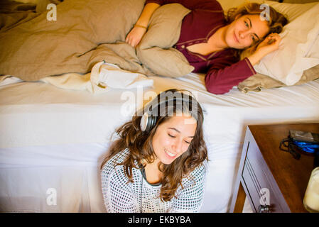 Two young female friends lying in bed and listening to headphones Stock Photo
