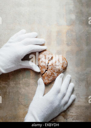 Gloved hands holding heart-shaped gingerbread cookie Stock Photo