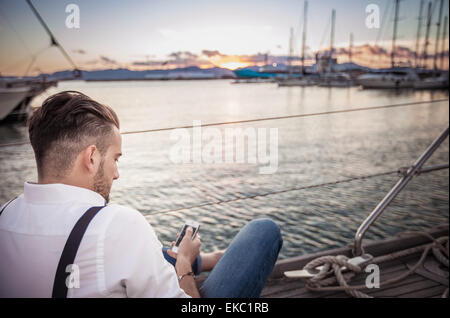 Young man using smartphone on yacht, Cagliari, Sardinia, Italy Stock Photo
