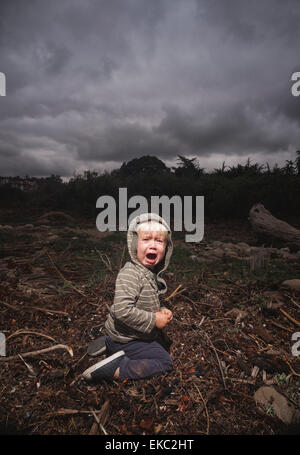 Young boy kneeling on ground crying against stormy sky Young boy kneeling on ground crying against stormy sky