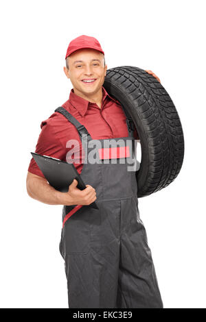 Vertical shot of a male manual worker in a gray jumpsuit holding a clipboard and a tire isolated on white background Stock Photo