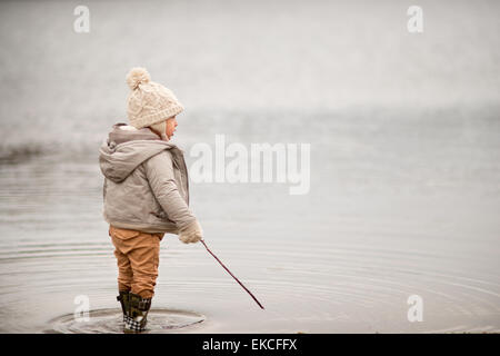 Young boy standing in a lake, holding a stick Stock Photo