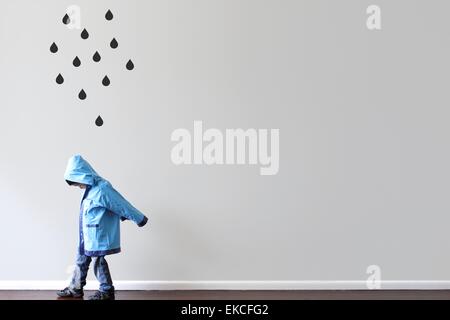 Boy in raincoat walking past a wall with black raindrops painted on the wall