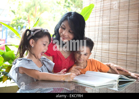 Asian mother with young daughter and son reading a story book together in a home environment Stock Photo