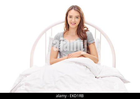 Studio shot of a beautiful brunette woman lying in a bed covered with white blanket and looking at the camera Stock Photo