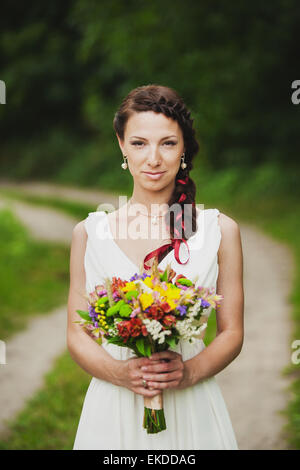 Young woman with bouquet of flowers in her hands standing in green summer park. Wedding decor. Bride with bright wedding bouquet Stock Photo