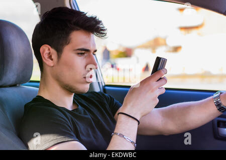 Distracted Young Man Using Cell Phone While Driving a Car Stock Photo